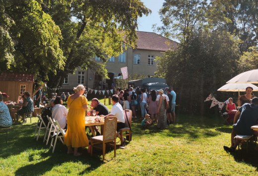 The MitsommerRemise in Klocksin Manor Park with food and drinks. People sit at tables in the park behind the manor house.