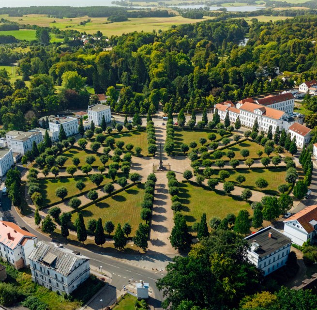 Aerial view of the Circus in Putbus on the island of Rügen, a circular square with symmetrically arranged trees and classicist buildings, surrounded by green nature and a rural landscape.