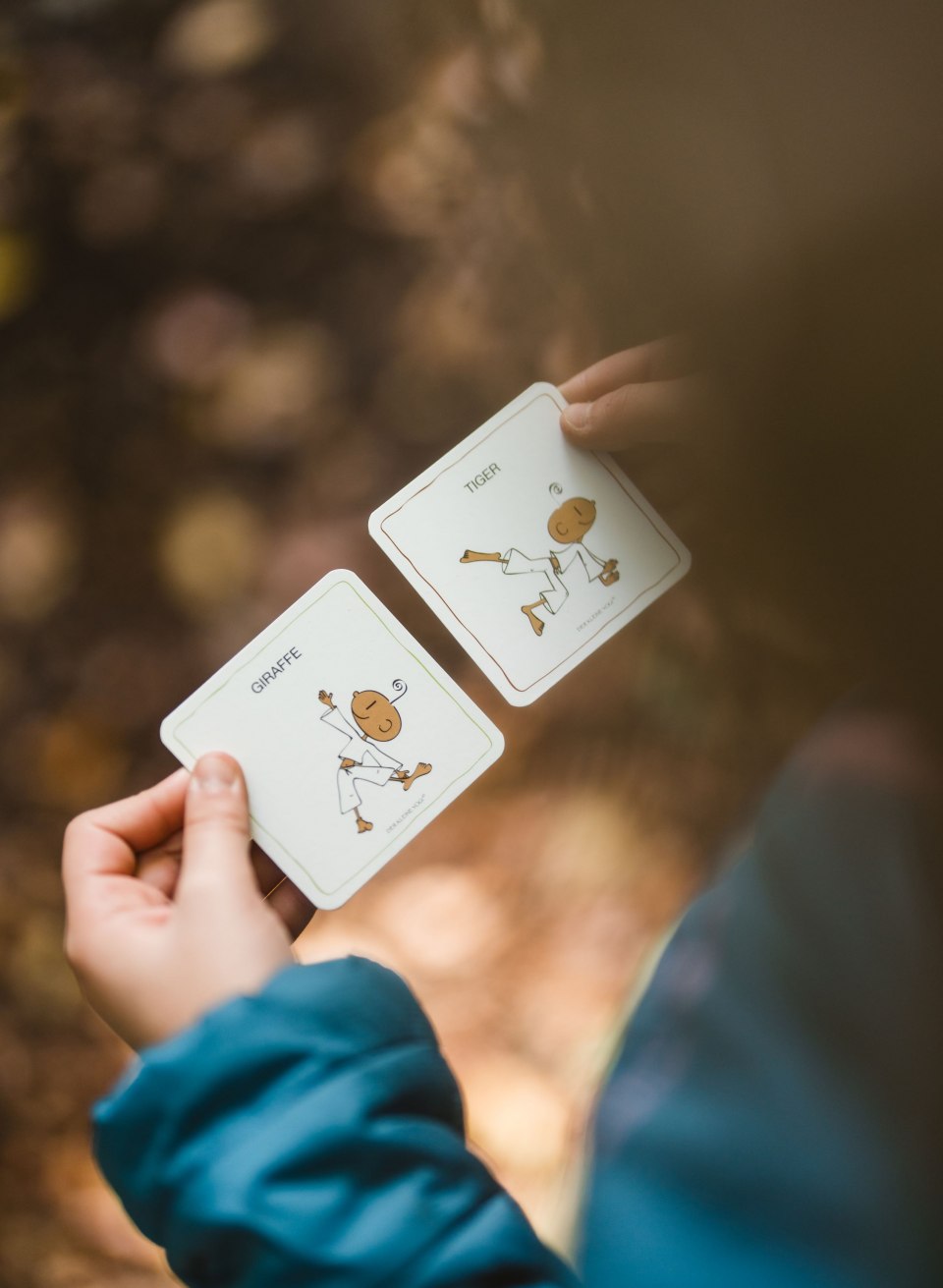 One person holds two yoga exercise cards showing postures such as "tiger" and "giraffe" with drawn figures.