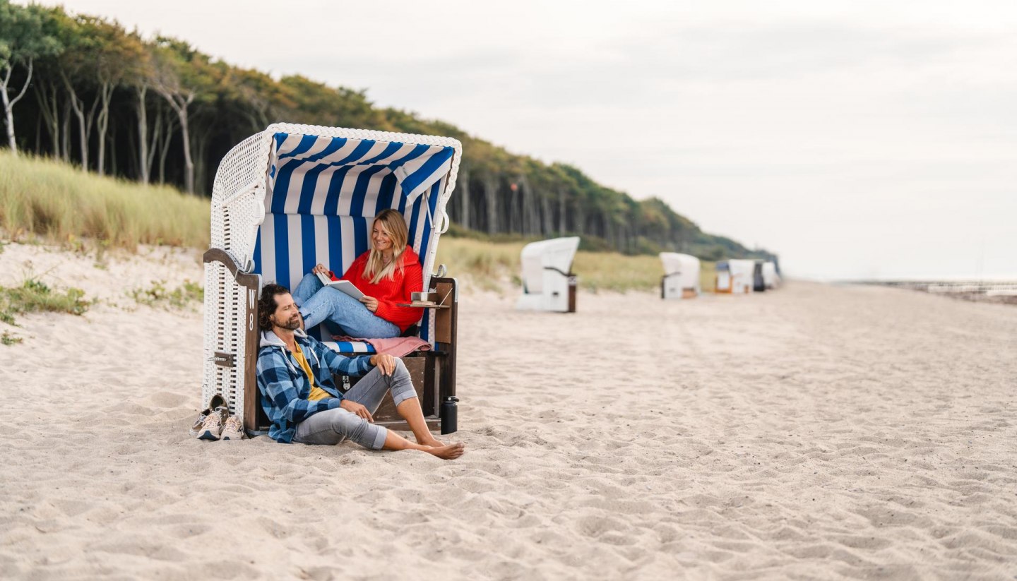 Couple sitting in a beach chair on the beach at Graal-Müritz on the Baltic Sea coast. The coastal forest can be seen in the background.