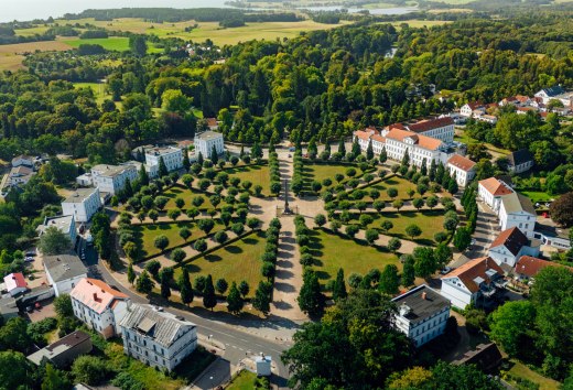 Aerial view of the Circus in Putbus on the island of Rügen, a circular square with symmetrically arranged trees and classicist buildings, surrounded by green nature and a rural landscape.