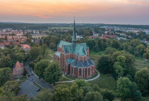 Aerial view of the cathedral in Bad Doberan at sunset, surrounded by trees, meadows and the surrounding town.