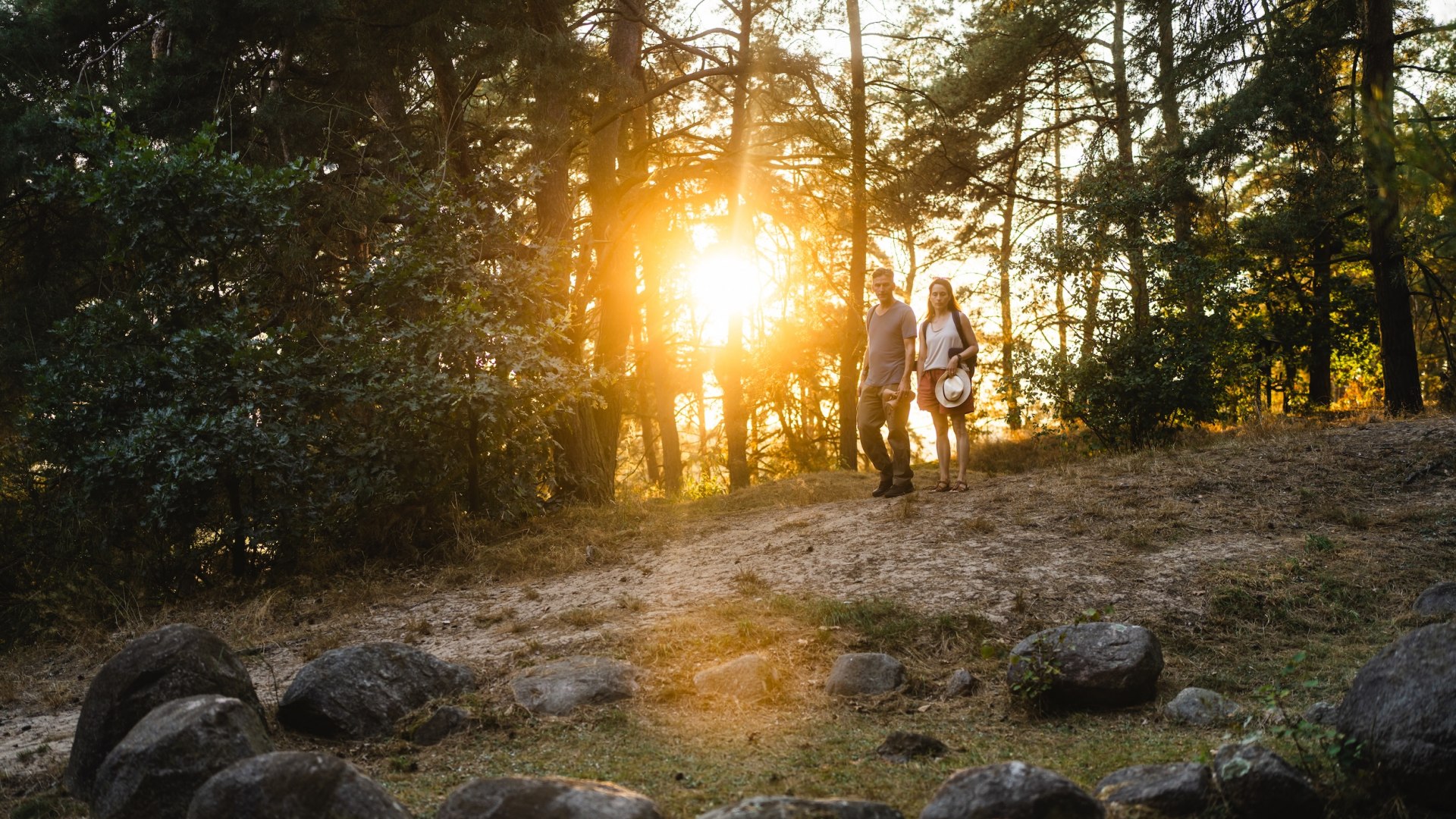 A couple walks at dusk to the historic Viking graves near Menzlin, surrounded by trees and warm light.