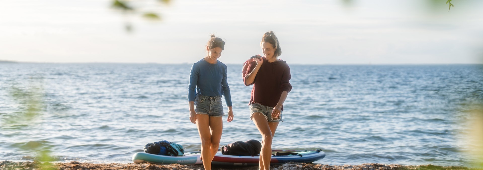 The sun is already low as the two friends pull their boards ashore on the small sandy beach in front of the Bolter Ufer campsite. Behind them, the Müritz almost looks like the sea., © TMV/Gross