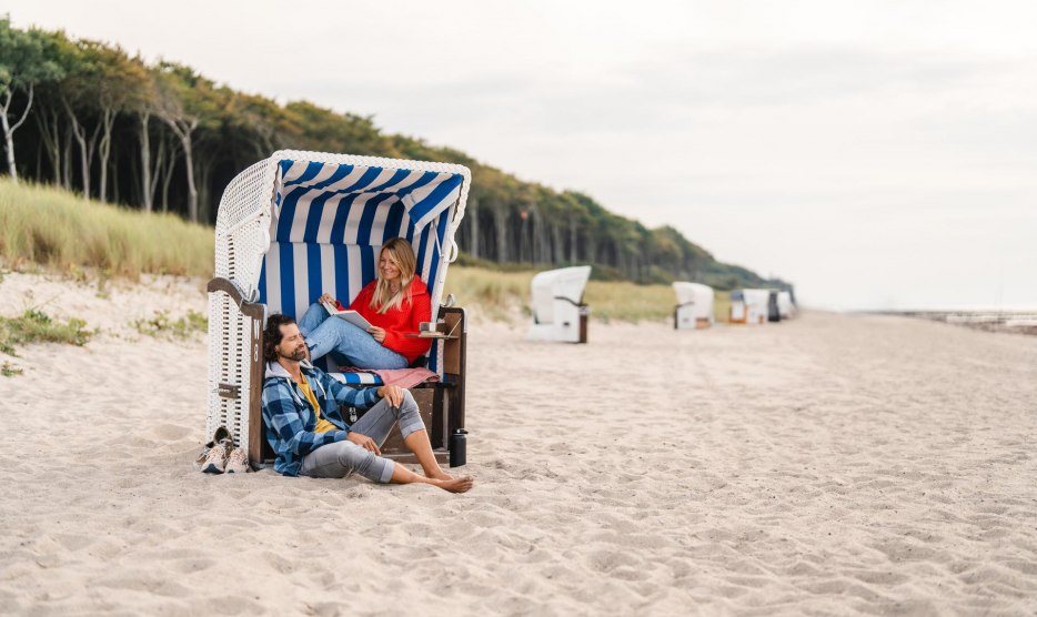 Couple sitting in a beach chair on the beach at Graal-Müritz on the Baltic Sea coast. The coastal forest can be seen in the background.