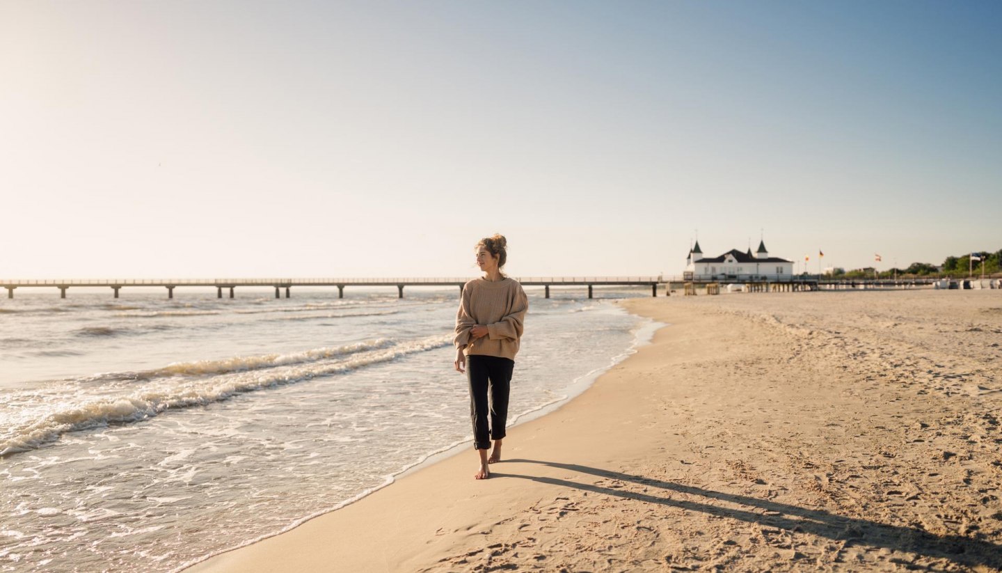 Woman walking on the beach of Ahlbeck at sunrise with pier in the background