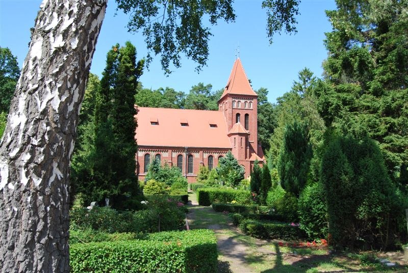 St. Luke's Church in Graal-Müritz, a red brick church with a tower, surrounded by green gardens and tall trees.