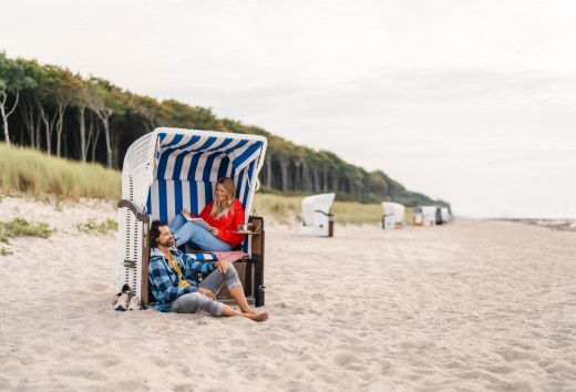 Couple sitting in a beach chair on the beach at Graal-Müritz on the Baltic Sea coast. The coastal forest can be seen in the background.