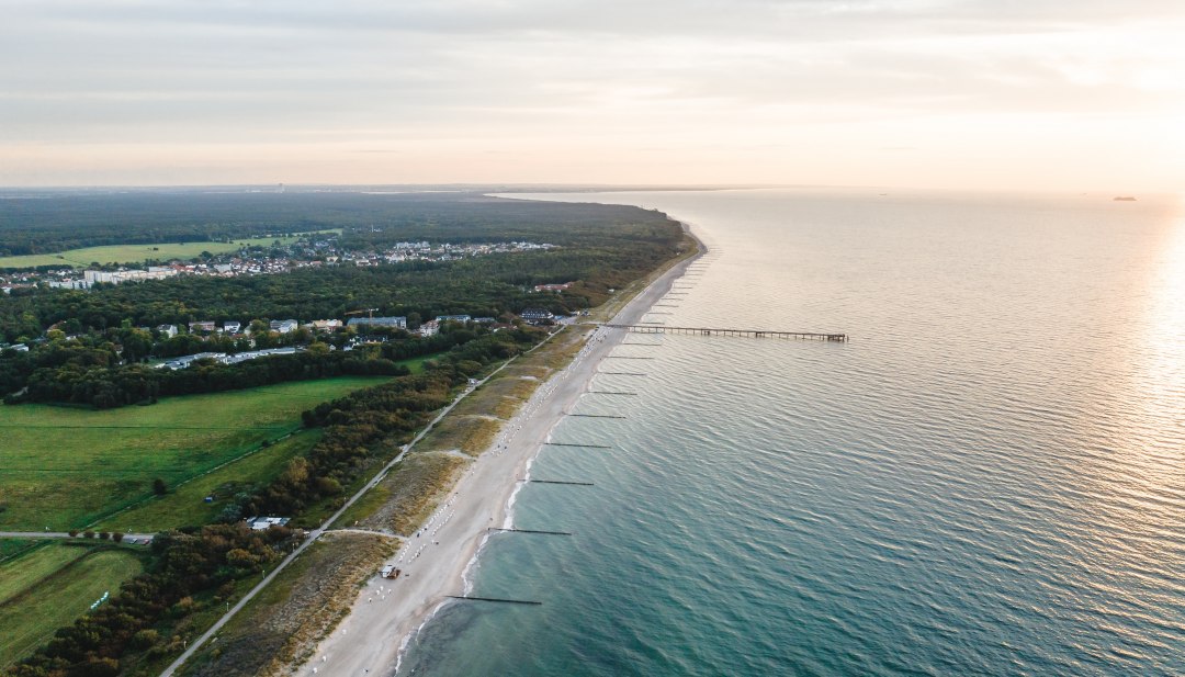 Aerial view of the pier and the beach of Graal-Müritz, surrounded by woods and meadows, with the Baltic Sea in the light of an atmospheric sunset.