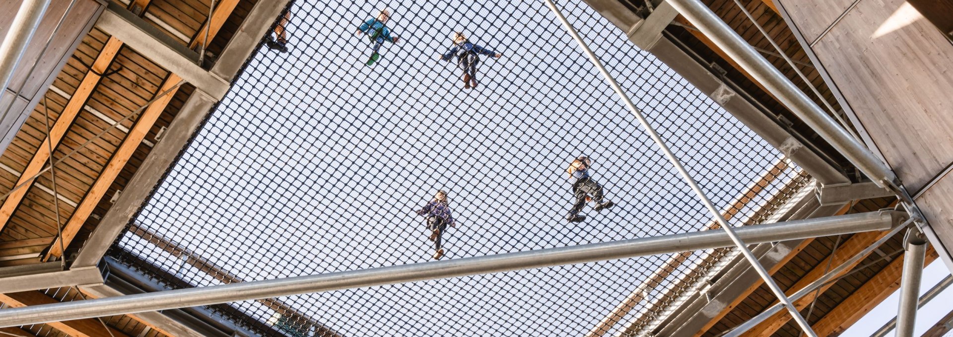 View from below through a large safety net in a wooden tower, on which several children are standing and playing.