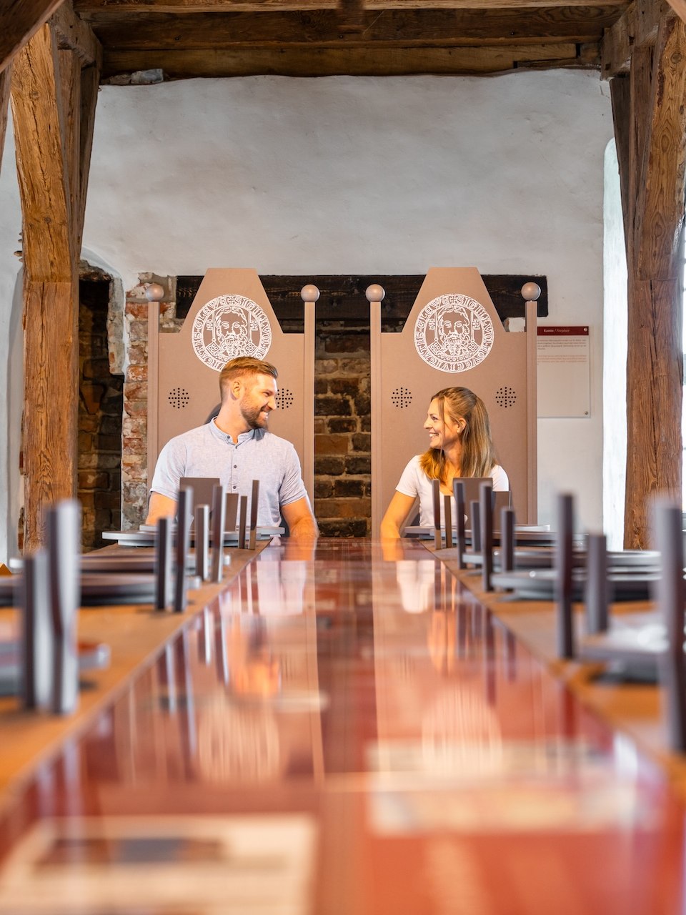 A couple sits at a long wooden table in the castle museum in Neustadt-Glewe, surrounded by old walls. They smile at each other and enjoy the historic atmosphere.