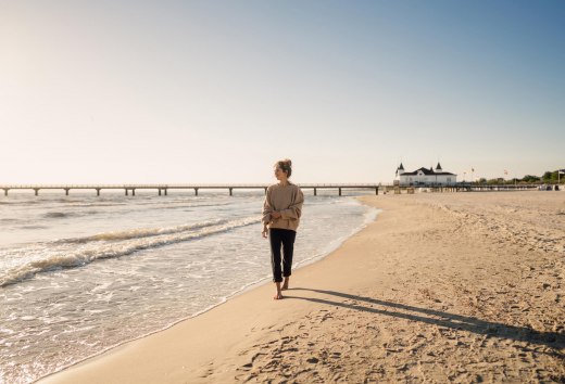 Woman walking on the beach of Ahlbeck at sunrise with pier in the background