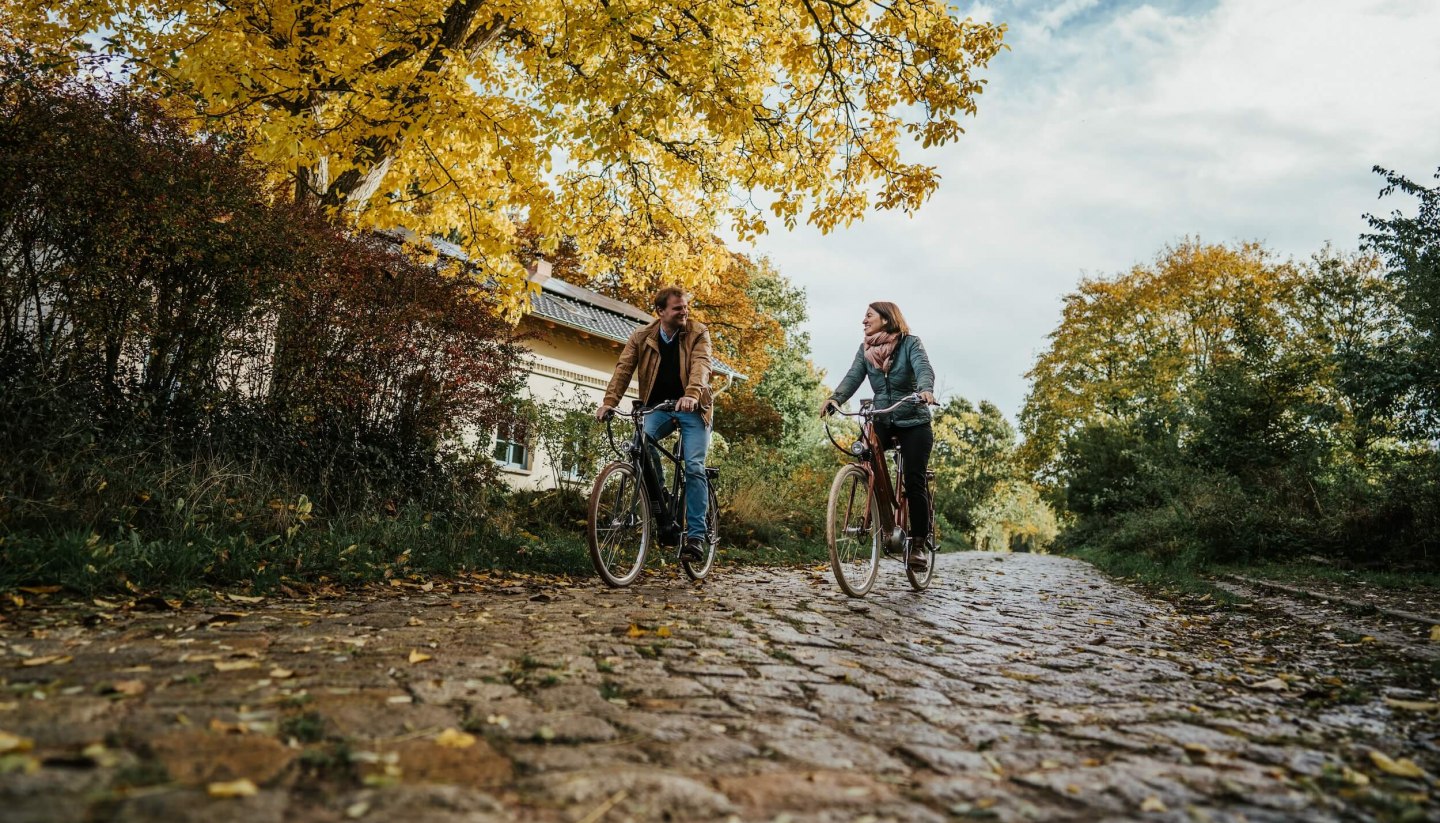 Two people cycling on cobblestones near the Pohnstorf estate in the fall.