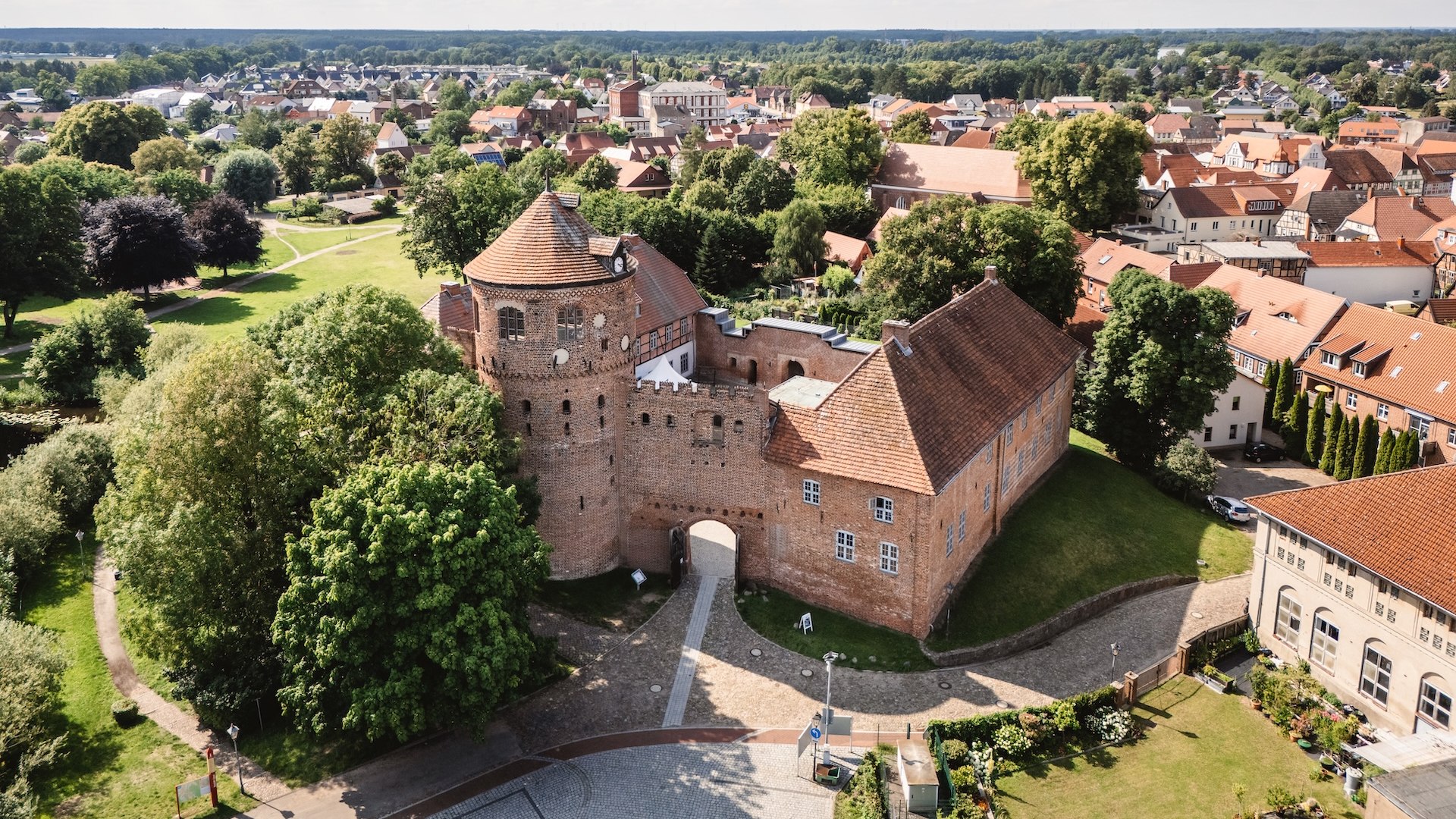 An aerial view of the historic Neustadt-Glewe castle, surrounded by green trees and the picturesque old town with its red-tiled roofs.