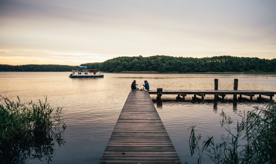 A relaxed picnic on a wooden jetty: surrounded by peaceful nature, people enjoy the tranquil atmosphere by the water.