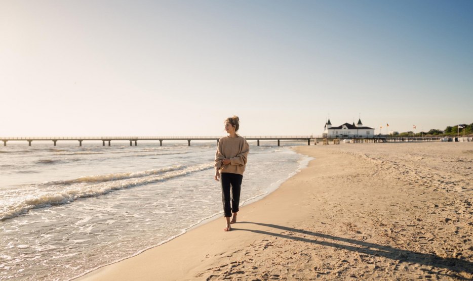 Woman walking on the beach of Ahlbeck at sunrise with pier in the background