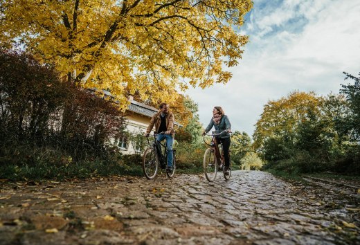 Two people cycling on cobblestones near the Pohnstorf estate in the fall.