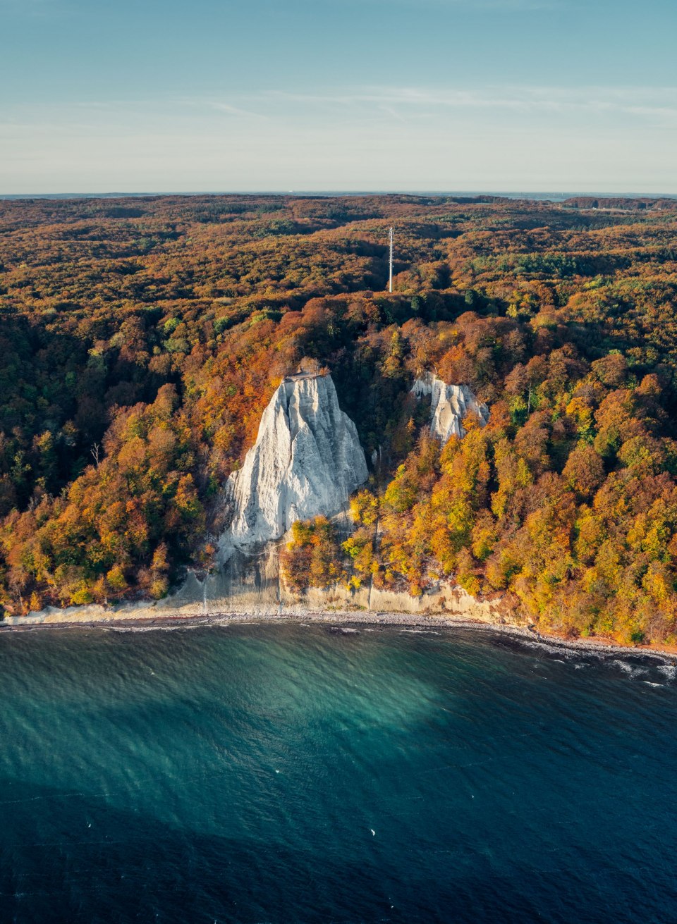 The imposing chalk cliffs in the Jasmund National Park glow in the morning autumn sun, surrounded by a sea of colorful foliage and the deep blue Baltic Sea - a breathtaking sight in the golden season.